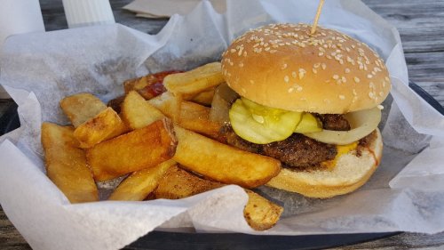 A sesame seed bun burger with pickles and onions, served with golden fries on a paper-lined tray.