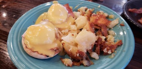 A blue plate with two eggs Benedict topped with hollandaise sauce and a side of crispy hash browns.