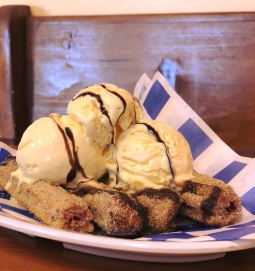 A plate of churros topped with three scoops of vanilla ice cream and drizzled with chocolate sauce.