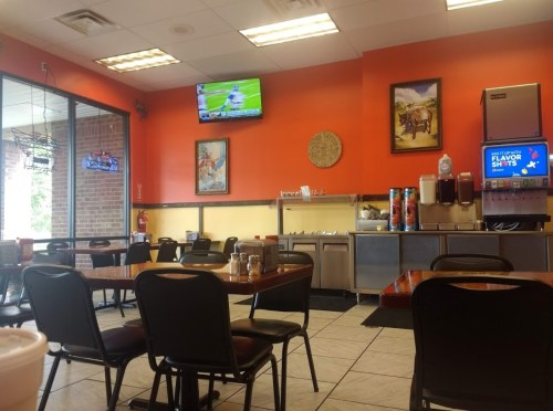 Interior of a casual restaurant with orange walls, tables, and a TV showing sports. Drink station in the background.