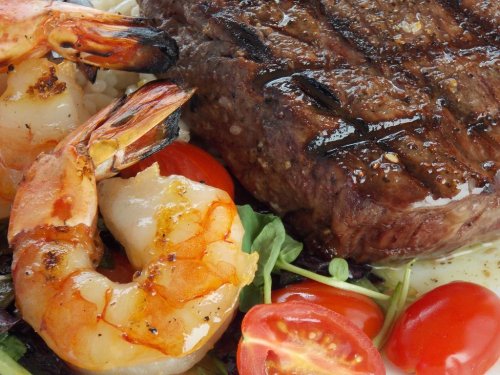 Grilled steak with shrimp, cherry tomatoes, and greens on a plate, showcasing a delicious surf and turf dish.