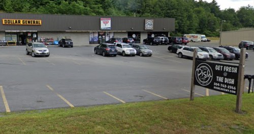 A parking lot with various cars in front of a Dollar General and a restaurant sign for "The Dish." Green trees in the background.
