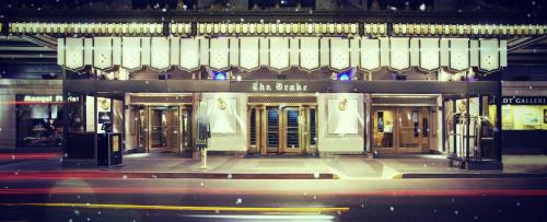 The ornate entrance of The Drake hotel, illuminated with lights, set against a snowy urban backdrop.