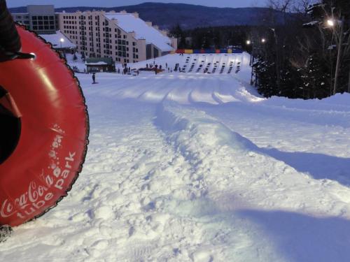 A snowy tubing hill with a red inner tube in the foreground and a resort in the background, illuminated at dusk.