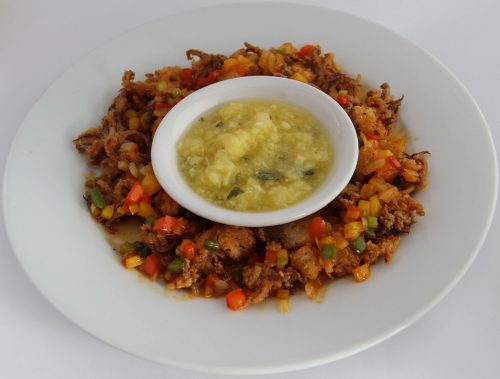 A plate of crispy fried food with colorful diced vegetables and a small bowl of sauce in the center.
