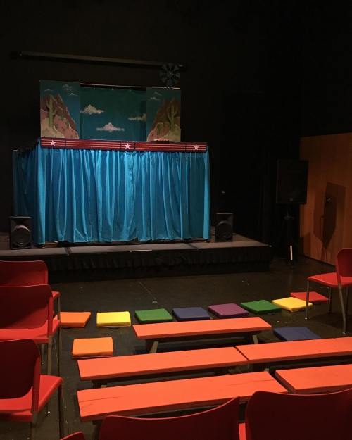 A small theater stage with a colorful backdrop, blue curtains, and orange, yellow, and purple seating in front.