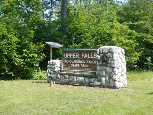 Sign for Upper Falls at Tahquamenon Falls State Park, surrounded by greenery and trees.