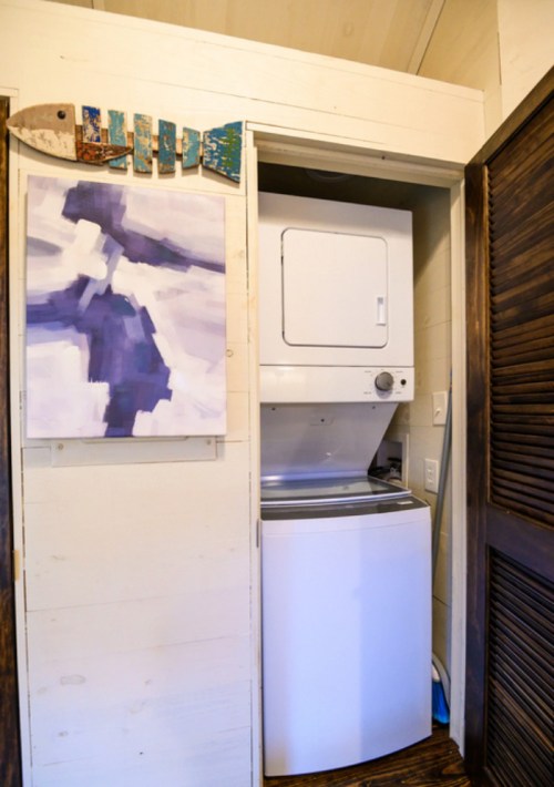 A compact laundry area featuring a stacked washer and dryer, with a colorful painting on the wall above.