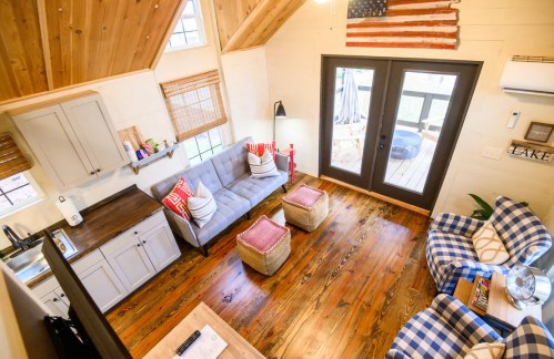 Cozy living room with wooden floors, a gray sofa, plaid chairs, and an American flag decor on the wall.