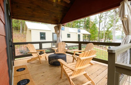 Cozy porch with wooden chairs and a fire pit, surrounded by trees and a view of a cabin in the background.