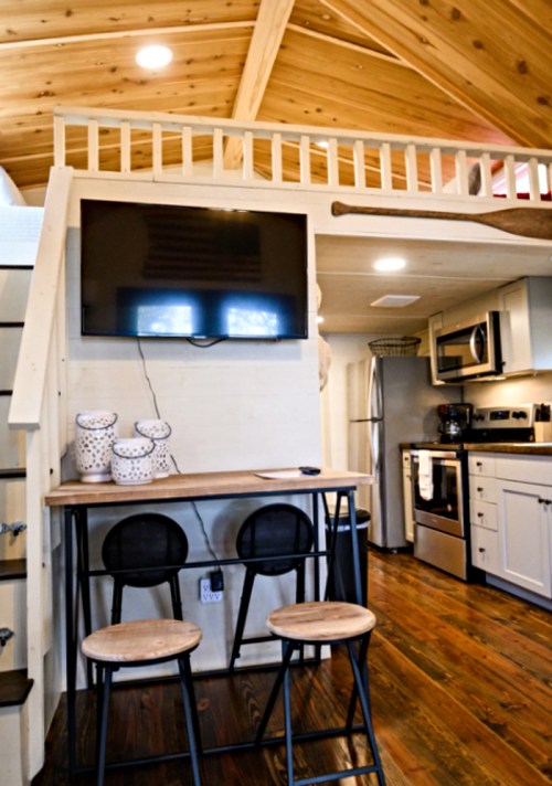 Cozy interior of a tiny home featuring a kitchen, dining area, and loft with wooden accents and modern appliances.