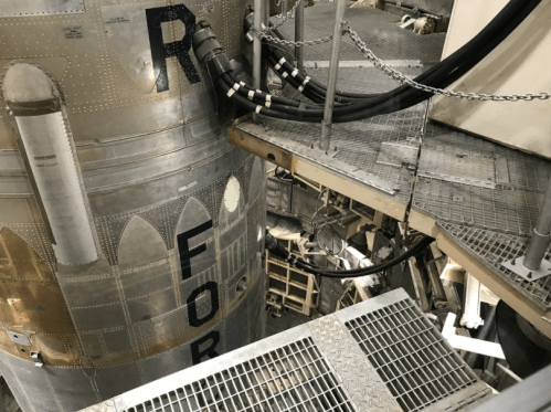 Close-up view of a rocket's metallic structure and surrounding platform, showcasing pipes and industrial details.