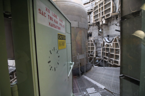 Interior of a missile silo with a caution sign and a large cylindrical structure in the background.