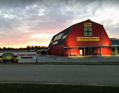 A red barn-style building with a sign for a general store and event center, set against a sunset sky.