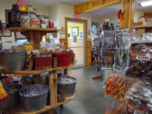 A cozy shop interior with wooden shelves filled with snacks and souvenirs, and a doorway leading to another area.
