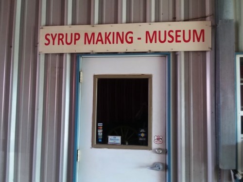 Sign above a door reading "Syrup Making - Museum" on a metal building.