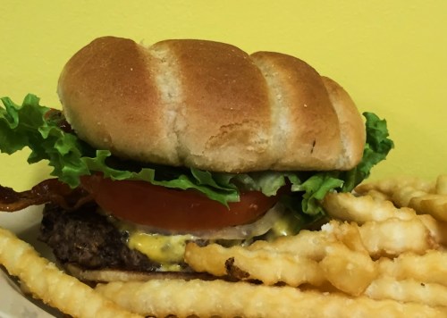 A delicious burger with lettuce, tomato, and cheese, served with crispy crinkle-cut fries on the side.