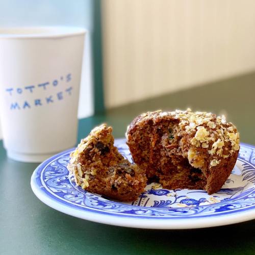 A blue plate holds a muffin with a bite taken out, next to a coffee cup labeled "Totto's Market."