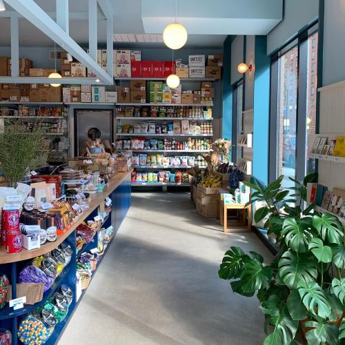 A bright, modern grocery store interior with shelves stocked with various snacks and products, and a plant in the foreground.