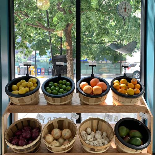 A display of fresh fruits in wooden baskets, including lemons, limes, oranges, and garlic, with a scale in the background.