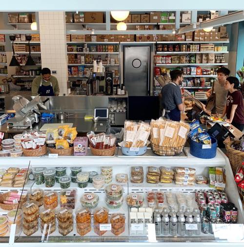 A vibrant market display with various packaged foods, snacks, and drinks, while customers interact with staff.