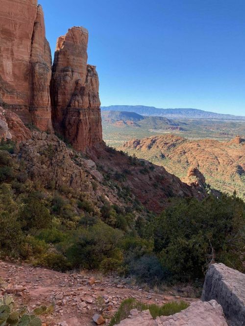 A scenic view of red rock formations and a lush valley under a clear blue sky.