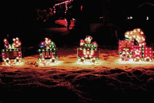 A festive train made of colorful lights and decorations, set against a snowy night backdrop.