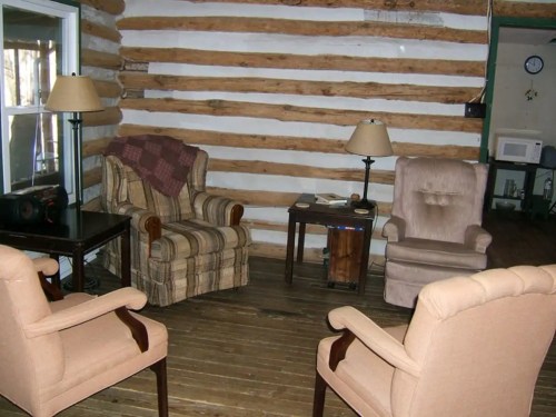 Cozy log cabin living room with two armchairs, a small table, and a rustic wooden floor.