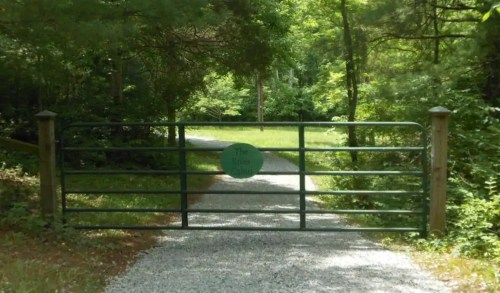 A green gate with a sign reading "The Ranch" leads to a gravel path surrounded by lush greenery.