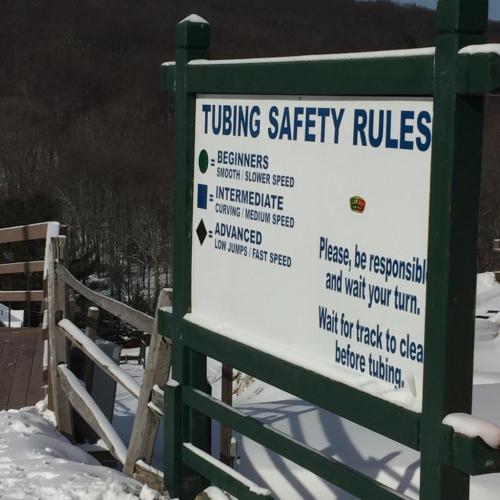 Sign displaying tubing safety rules: Beginners, Intermediate, and Advanced levels with speed and jump guidelines. Snowy background.