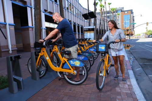 A man and woman are renting bikes from a bike-sharing station in an urban area.