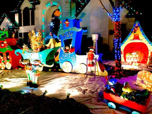 Colorful holiday display featuring a decorated train, festive characters, and a cozy house, all illuminated with lights.