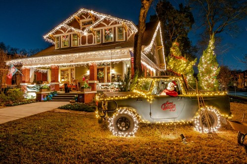 A festive house decorated with lights, featuring a vintage truck adorned with Christmas lights and a Santa figure.