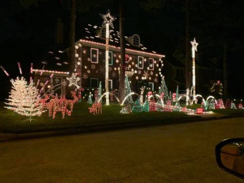 A beautifully decorated house with colorful Christmas lights, featuring trees, reindeer, and festive displays at night.