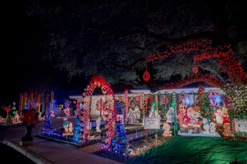 A festive house decorated with colorful Christmas lights, inflatables, and holiday decorations in a nighttime setting.