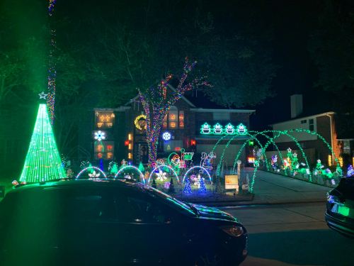 A house decorated with colorful Christmas lights, featuring a large green tree and various festive displays in the yard.