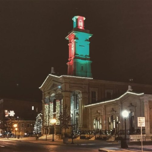 Historic building illuminated with green and red lights at night, adorned with festive decorations and a Christmas tree.