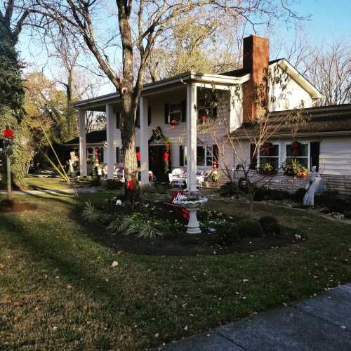 A charming house decorated for the holidays, featuring wreaths and red bows, surrounded by a lush garden.