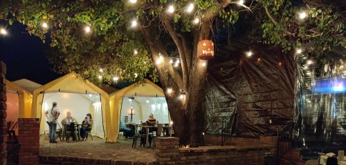 Cozy outdoor dining area with illuminated tents, string lights, and a tree, creating a warm evening atmosphere.