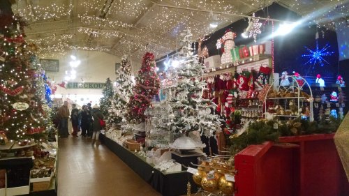 A festive holiday market filled with decorated trees, lights, and various Christmas decorations and gifts.