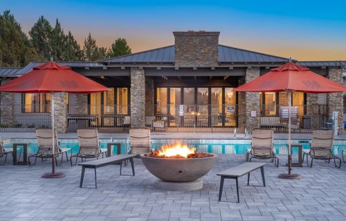 A cozy outdoor pool area with a fire pit, lounge chairs, and red umbrellas, set against a sunset backdrop.
