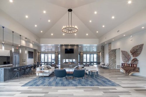 Modern lounge area with high ceilings, stylish furniture, and a large chandelier, featuring stone accents and a cozy atmosphere.