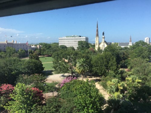 A view of a green park with trees, a church steeple, and buildings in the background under a clear blue sky.