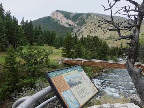 A scenic view of a river with a sign, surrounded by lush greenery and mountains in the background.