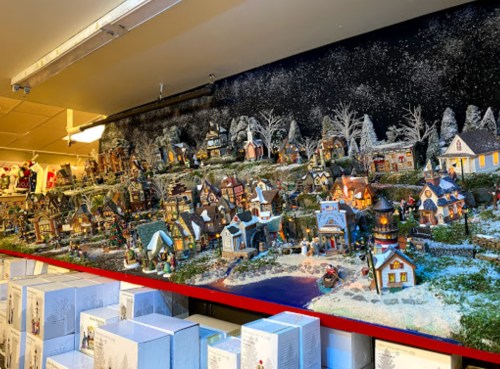A festive miniature village display with snow-covered houses, trees, and a pond, set against a starry night backdrop.