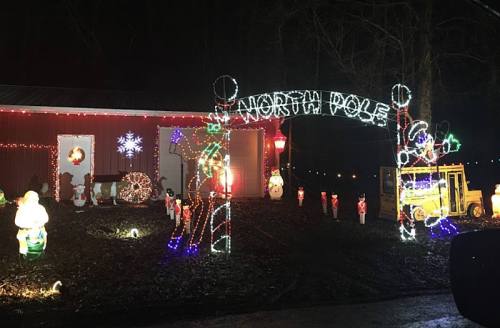 A festive display featuring a "North Pole" archway, colorful lights, and various holiday decorations outside a building.