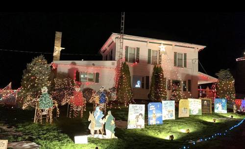 A house decorated with colorful Christmas lights and festive displays, including illuminated figures and storybook scenes.