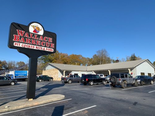 Exterior of Wallace Barbecue restaurant with a large sign, surrounded by parked cars and a clear blue sky.