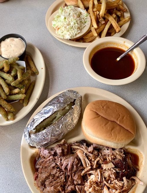 A plate of pulled pork with a baked potato, a bun, coleslaw, fries, and a side of green beans.