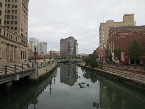 A cityscape featuring a canal, buildings, and reflections on the water under a cloudy sky.